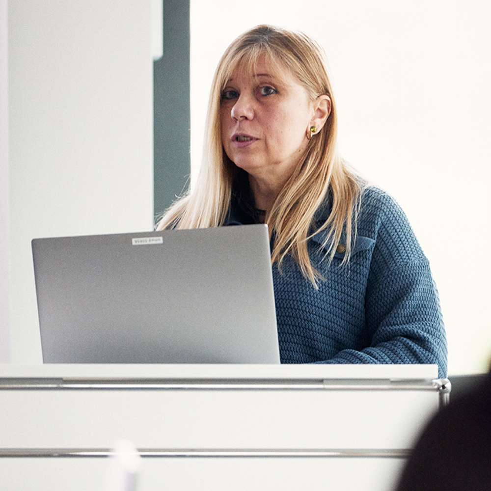 Eine Lehrende mit Laptop steht an einem Redepult.