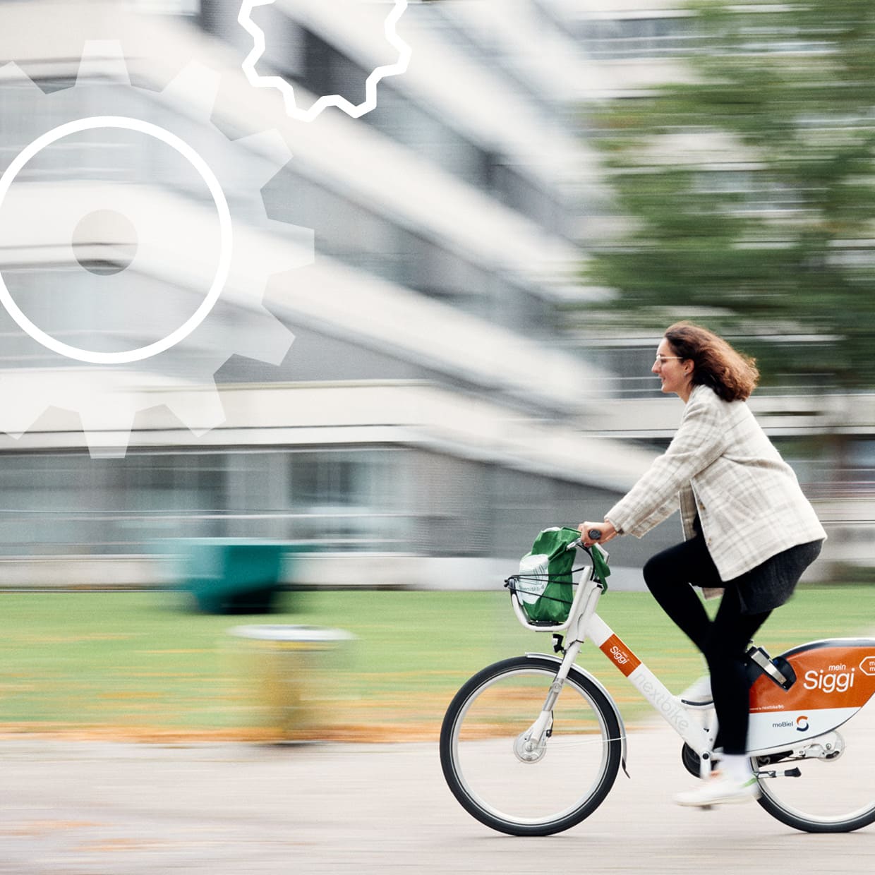 Person auf einem Siggi-Bike fährt vor der Uni entlang. Der Hintergrund ist verschwommen. Im Vordergrund sind symbolische Zahnräder.