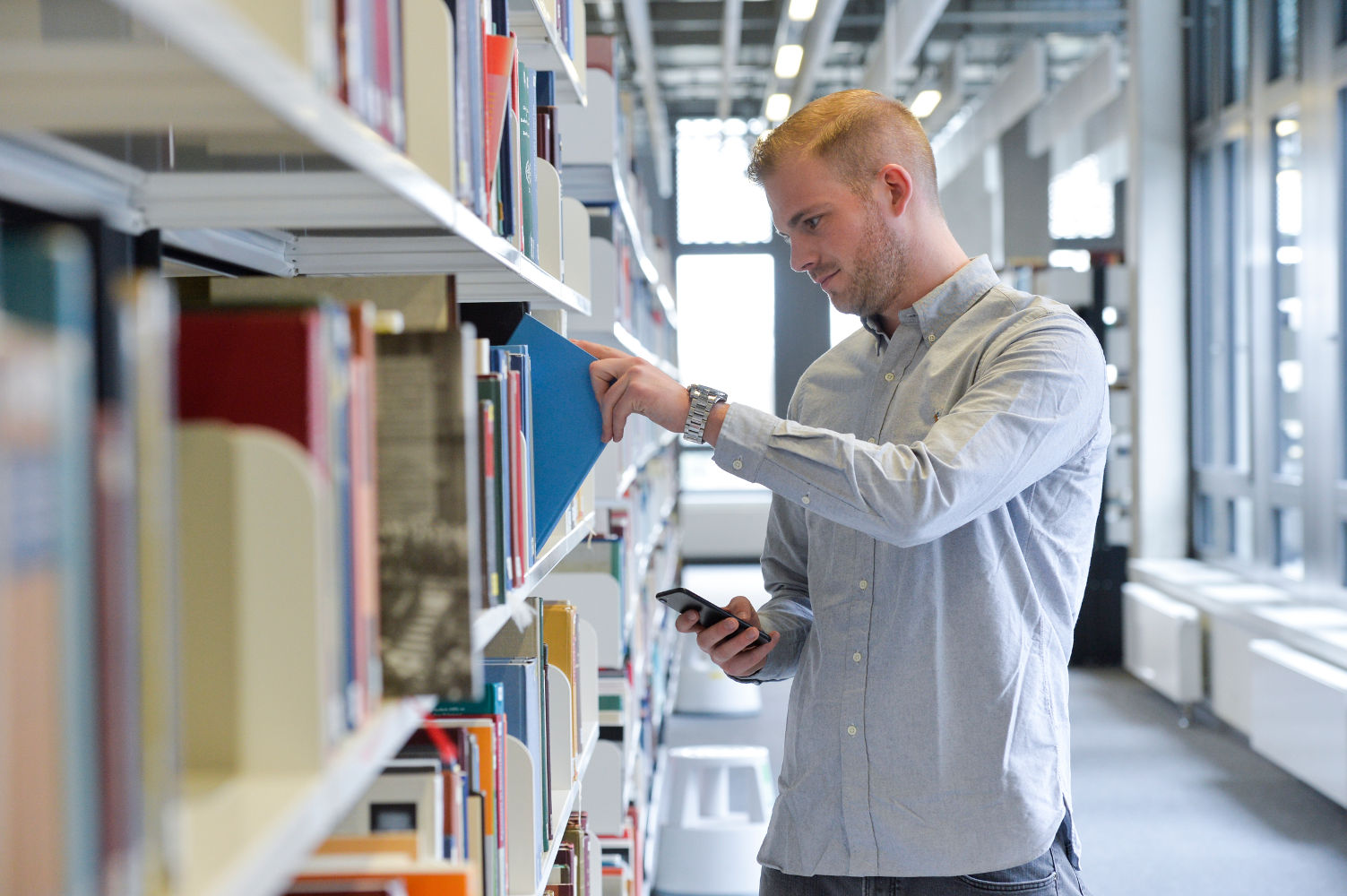 Person am Bücherregal mit Smartphone in der Hand