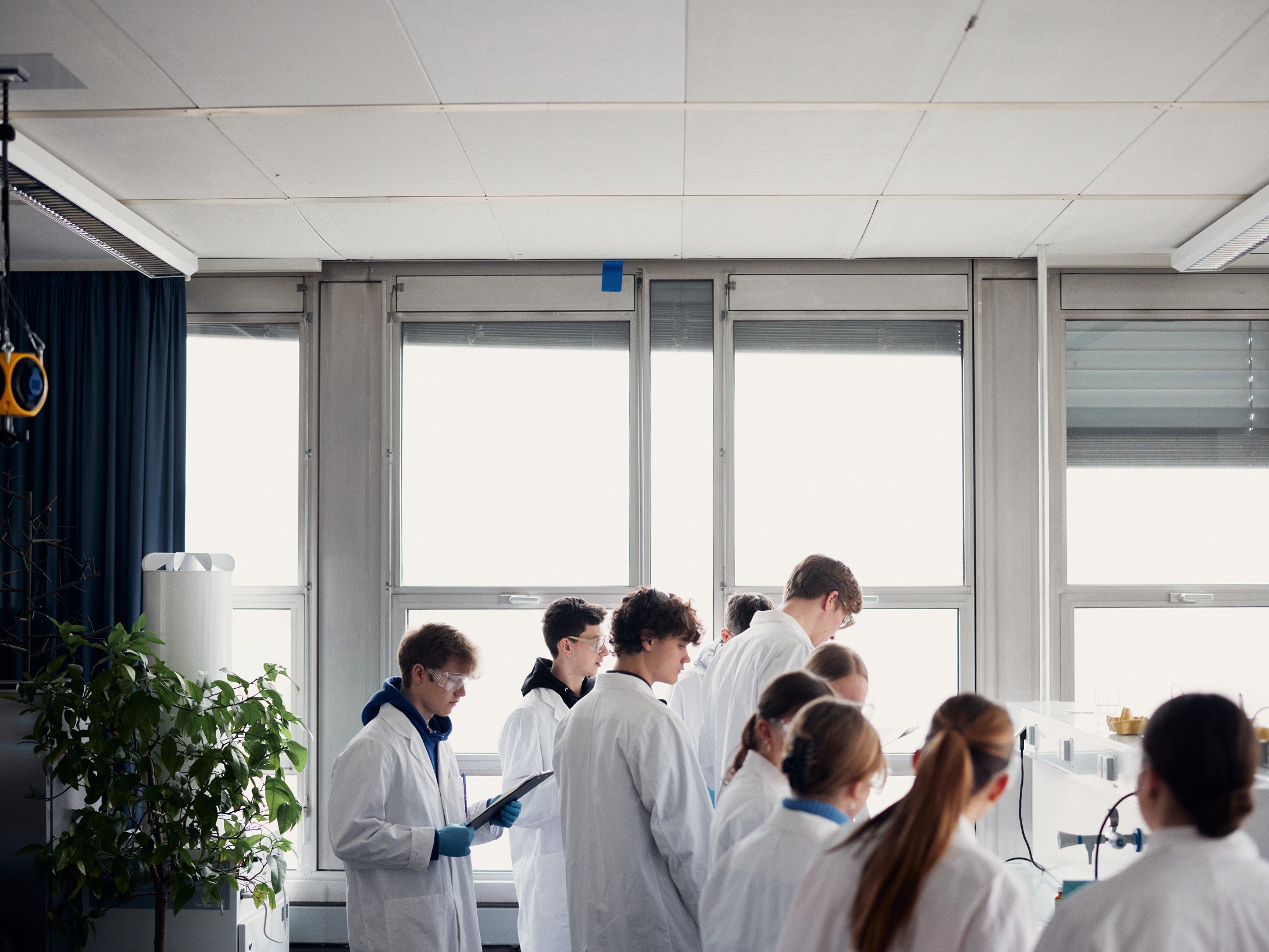 Eine Gruppe Jugendlicher steht in weißen Laborkitteln an einem Labortisch