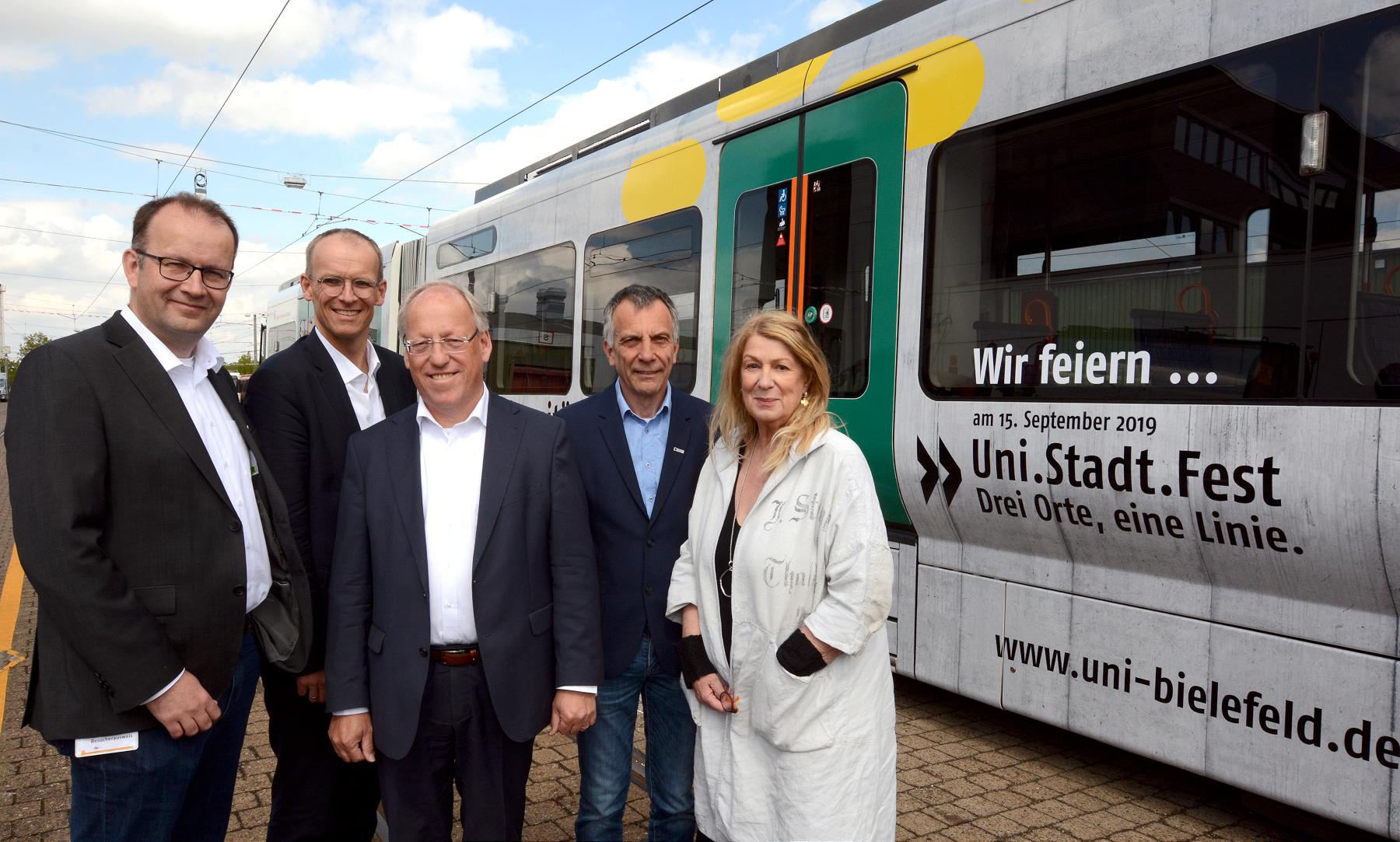 Auf dem Bild sind Martin Knabenreich (Geschäftsführer Bielefeld Marketing GmbH), Martin Uekmann (Geschäftsführer der Stadtwerke Bielefeld), Pit Clausen (Oberbürgermeister der Stadt Bielefeld), Prof. Dr.-Ing. Gerhard Sagerer (Rektor der Universität Bielefeld) und Jutta Küster (stellv. Vorsitzende Absolventen-Netzwerk) zu sehen. Sie stehen vor der  Jubiläumsbahn.