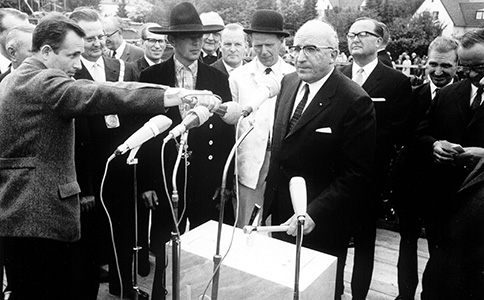 Schwarzweiß Foto von Heinz Kühn, der in zahlreiche Mikros spricht