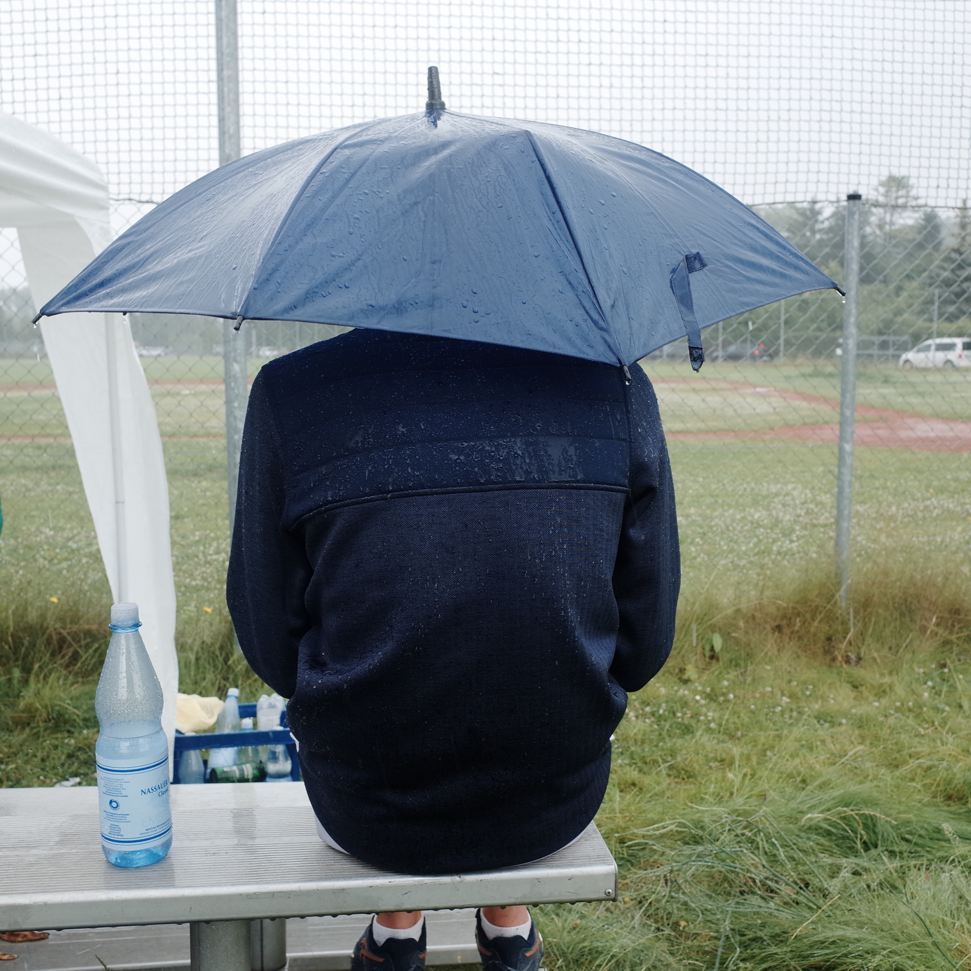 ein Spieler der Beavers sitzt mit Regenjacke und Schirm auf einer Bank