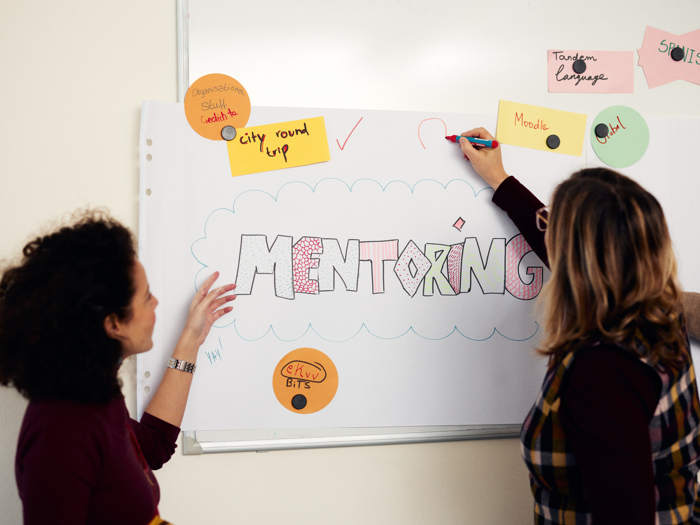 Zwei Personen stehen vor einem Plakat auf dem das Wort Mentoring steht