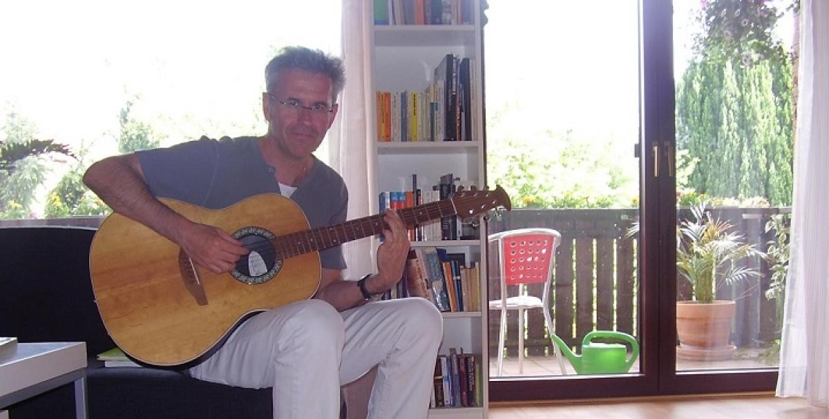 Photo of Willy Raussert playing the guitar and smiling into the camera