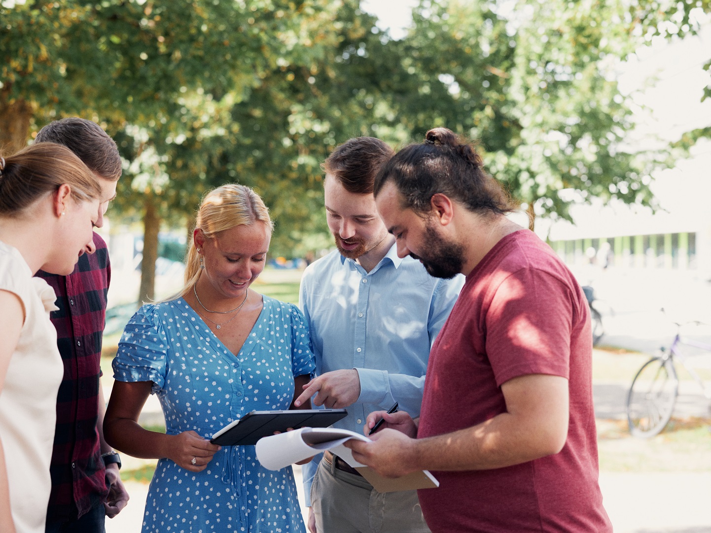 Fünf Personen stehen draußen im Kreis und deuten auf einen Tablet-PC