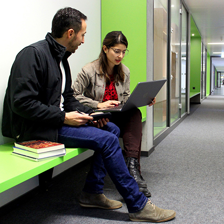 Foto mit einer Studentin und einem Studenten, die Gemeinsam in einer Sitzecke im Gang des CIAS an einem Laptop und mit Büchern lernen