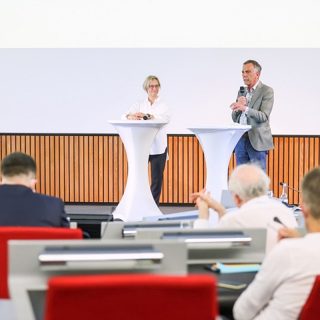 Prof'in Dr. Angelika Epple und Prof. Dr. Gerhard Sagerer stehen an Pulten auf einer Bühne vor Publikum