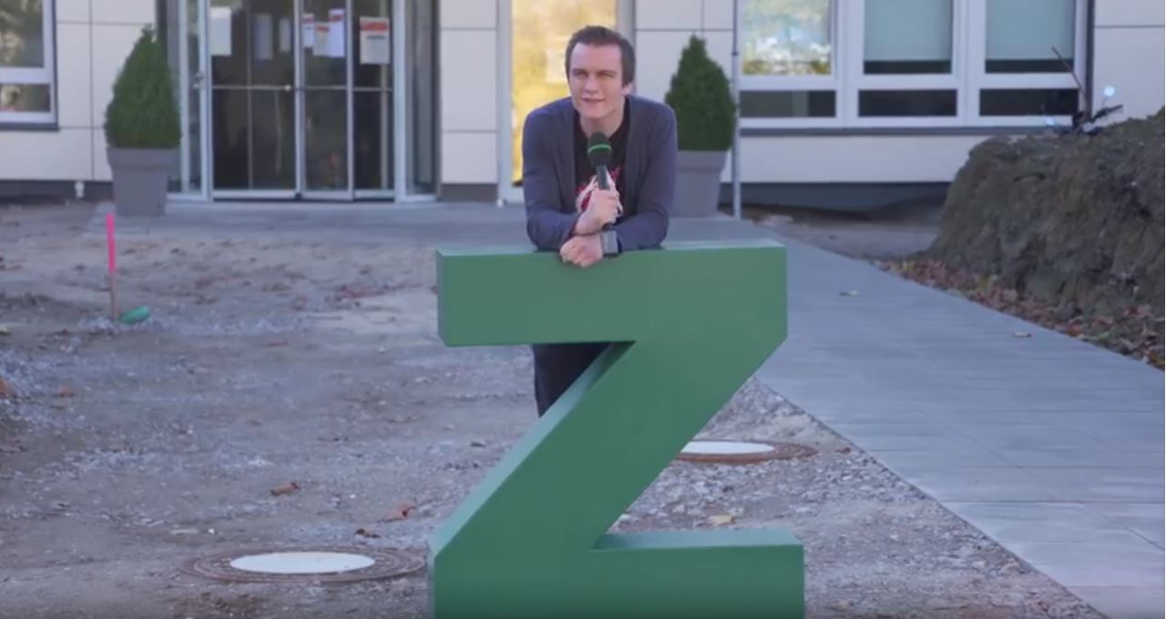 Moderator lehnt an dem großen Buchstaben "Z", das vor dem neuen Gebäude steht